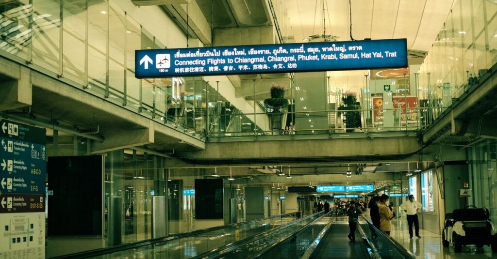 Photo: traveler walking briskly toward the Suvarnabhumi Airport Rail Link gates carrying only a phone and passport, roll