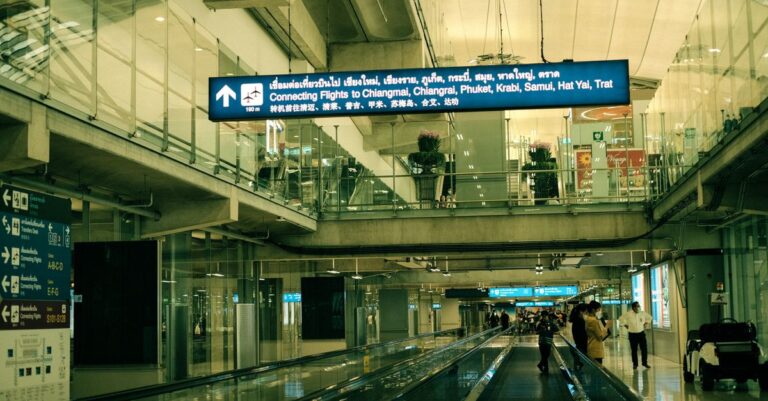 Photo: traveler walking briskly toward the Suvarnabhumi Airport Rail Link gates carrying only a phone and passport, roll