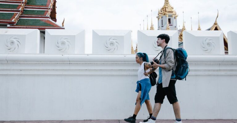 Travelers walking hands-free with small daypacks past Thai temple architecture