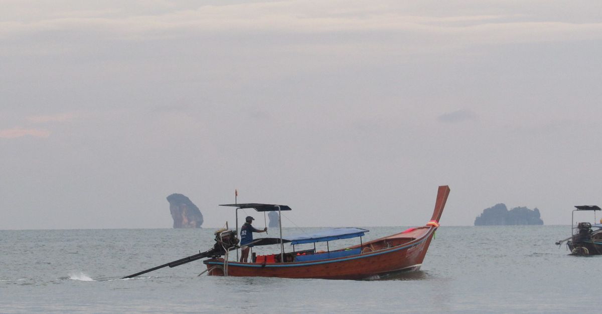 Traveler wading ashore from a longtail boat in Thailand with just a daypack