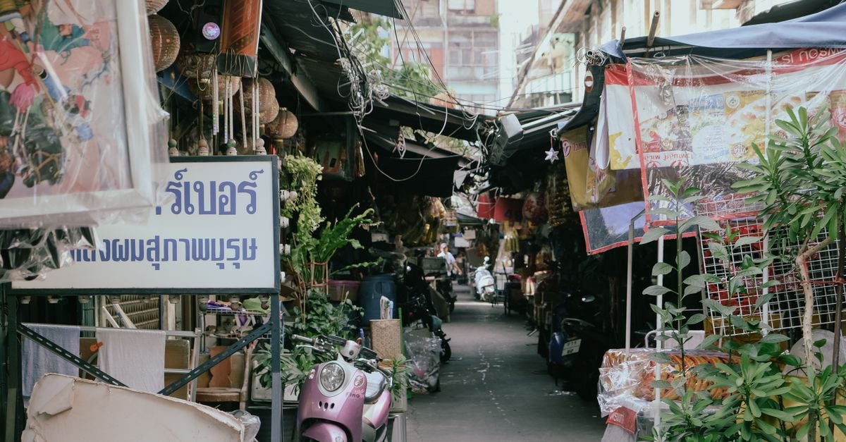 A narrow market alley crowded with stalls, awnings and parked motorbikes