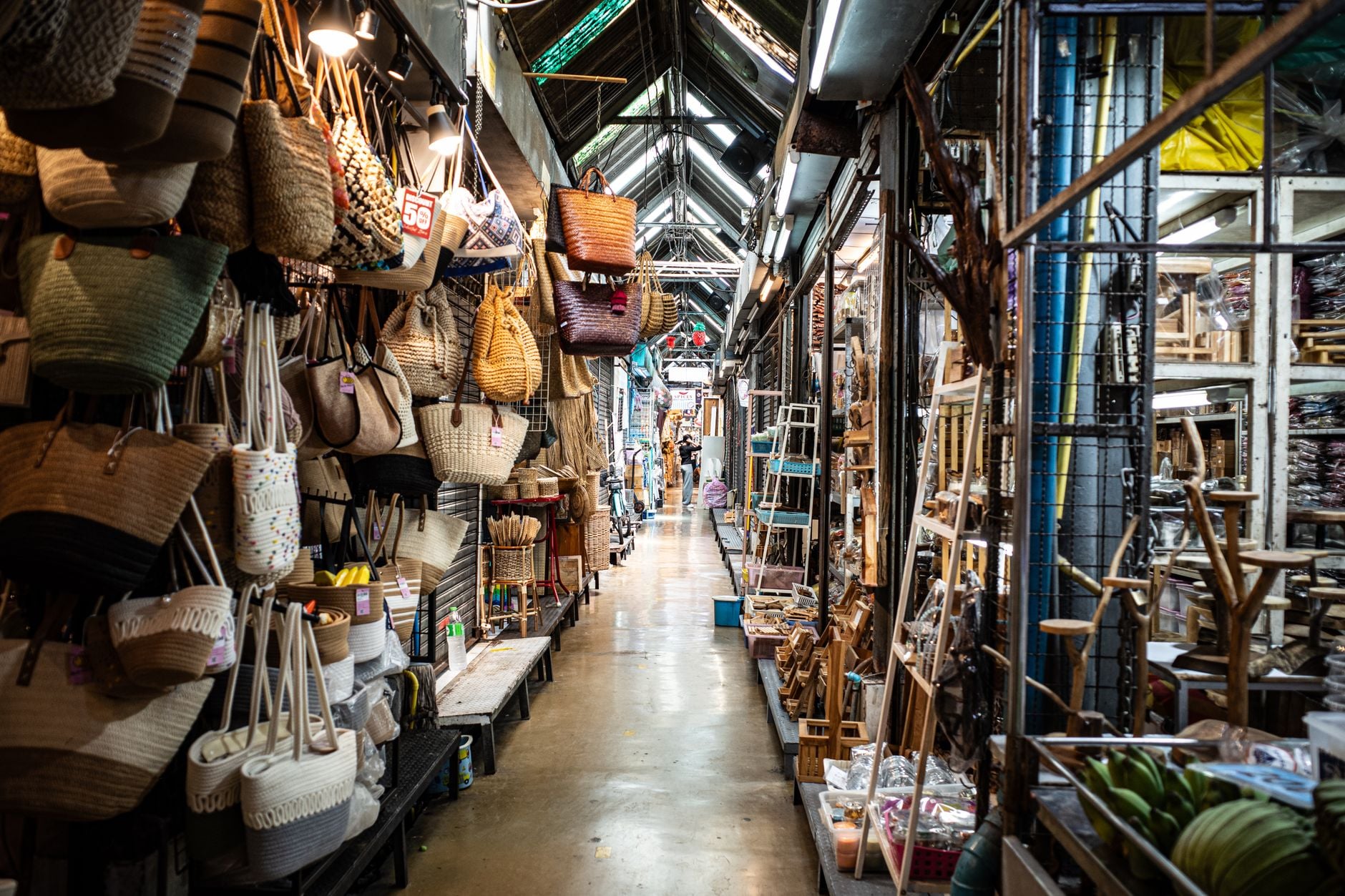 A covered market aisle at Chatuchak hung with woven bags and stacked with handicraft stalls on both sides