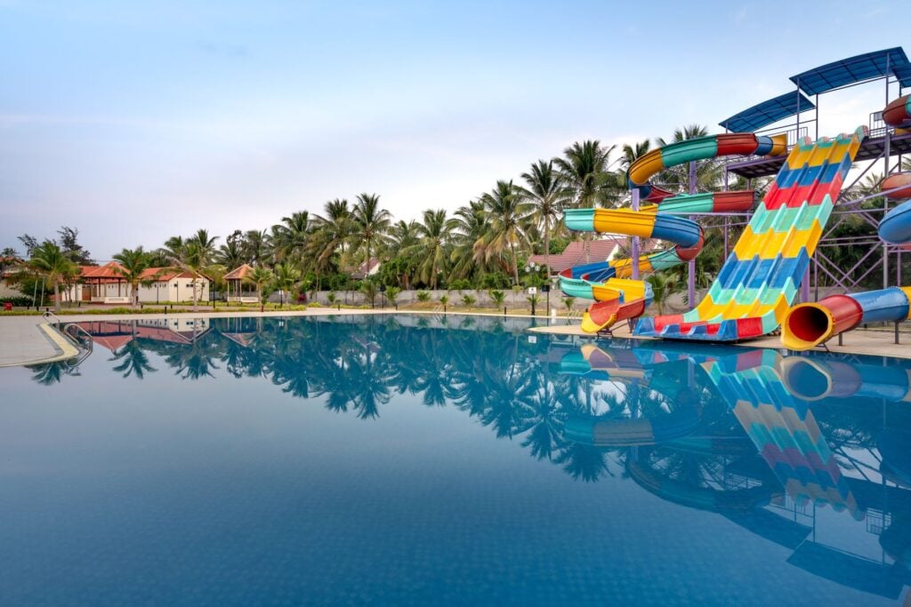 Colourful water slides beside a still blue pool, with palm trees behind