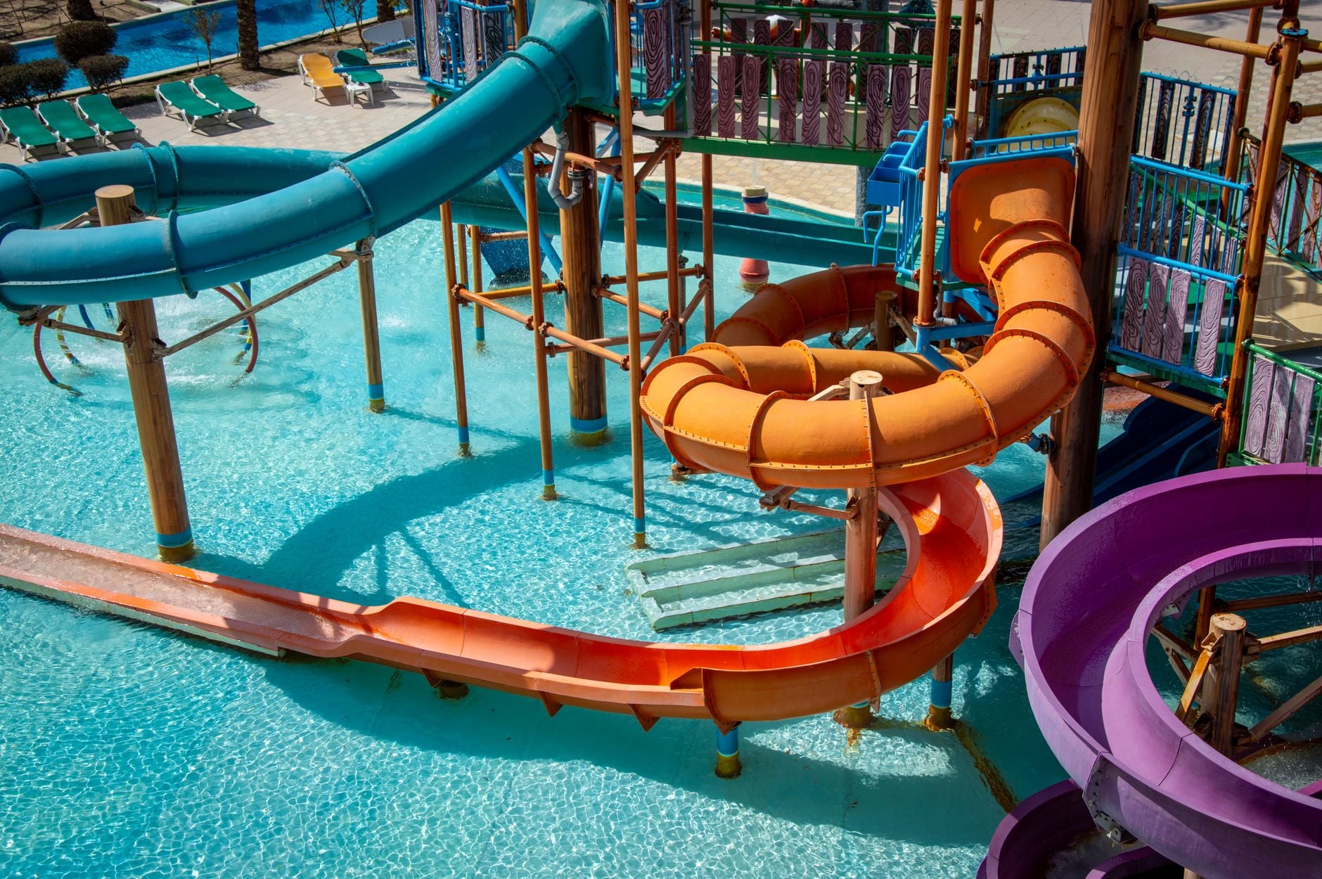 A shallow turquoise pool with a childrens water play structure, small slides and climbing frames