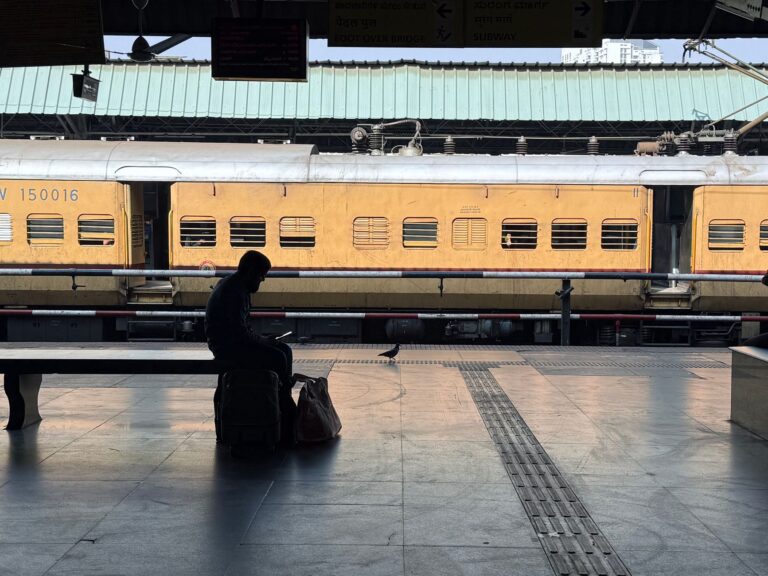 A traveller sitting on their suitcase on a station platform beside a yellow train