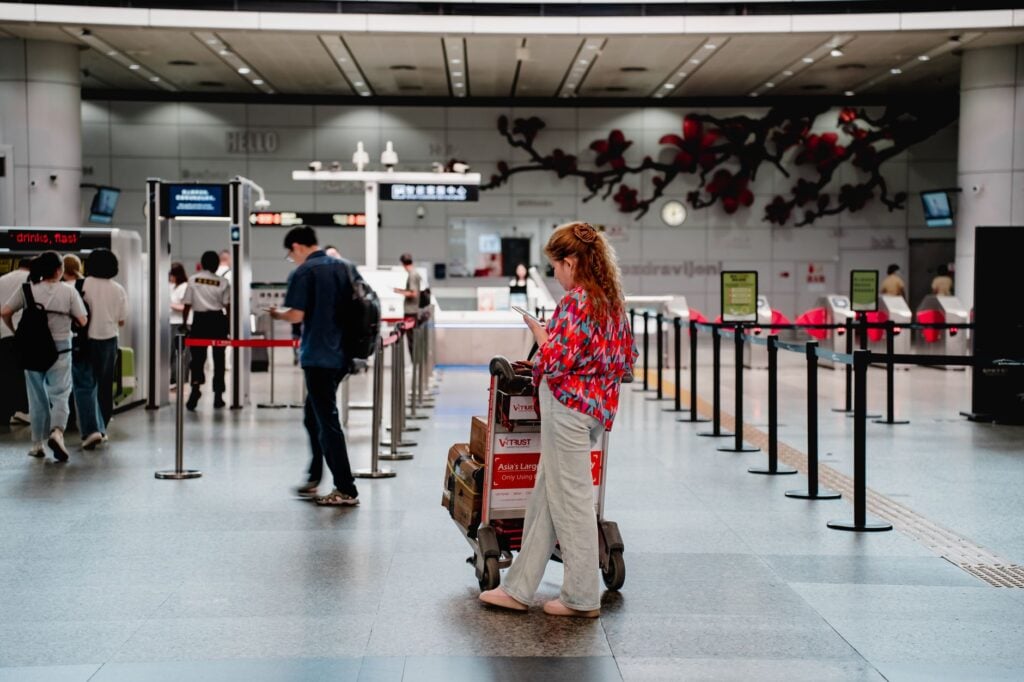 Traveller waiting beside a loaded luggage trolley in a check-in hall