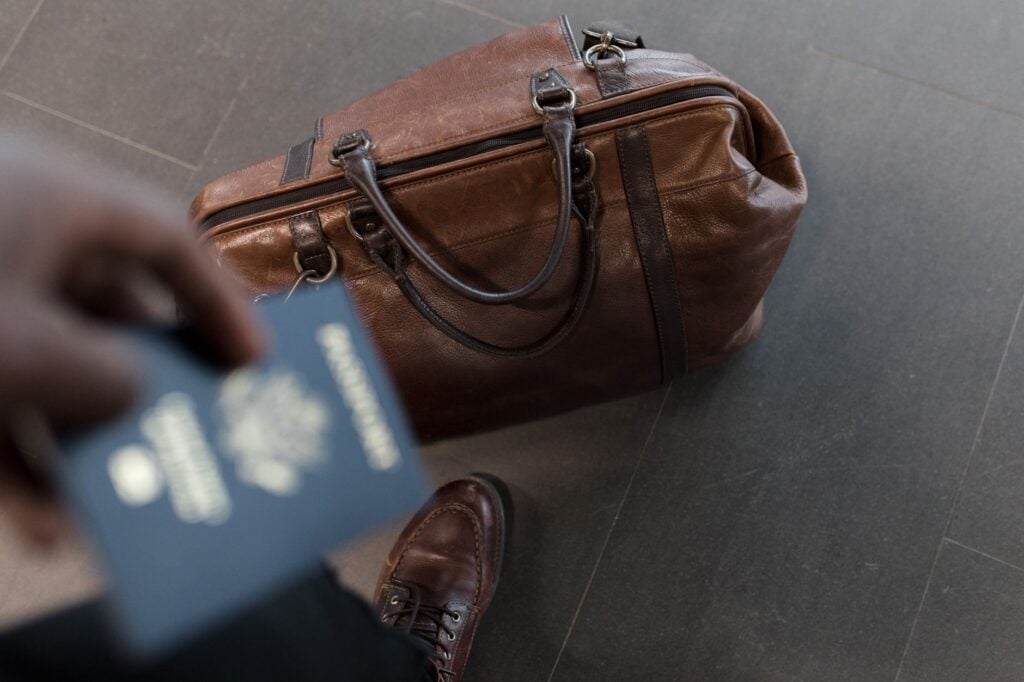Passport held beside a leather holdall bag before a flight