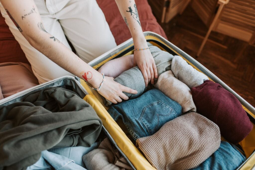 Hands packing folded clothes into an open suitcase