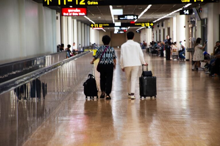 Two travellers wheeling suitcases along a terminal corridor signed for Gates 11 and 12